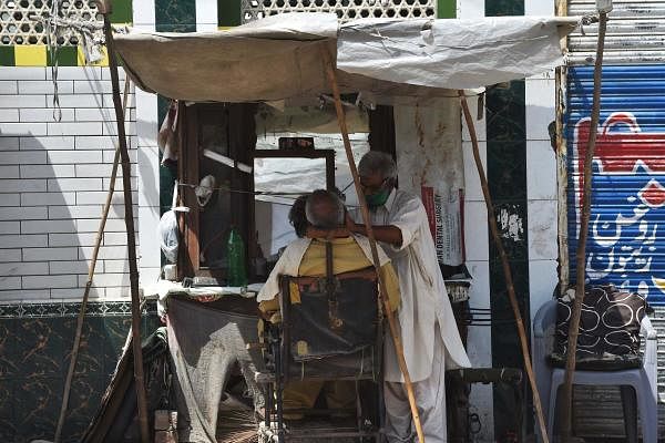 A street barber wearing a facemask gives a haircut to a customer during a government-imposed nationwide lockdown as a preventive measure against the COVID-19 coronavirus. (Credit: AFP Photo)