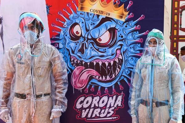 Policemen pose for photos wearing Personal Protective Equipment (PPE)standing next to a poster depicting the COVID-19 coronavirus during an event in Amritsar on April 16, 2020. (Credit: AFP Photo)