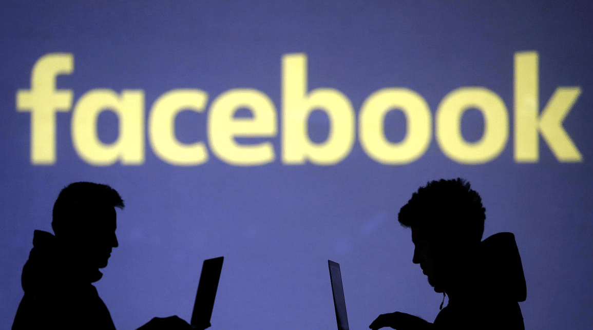 Silhouettes of laptop users are seen next to a screen projection of a Facebook logo (Reuters File Photo)