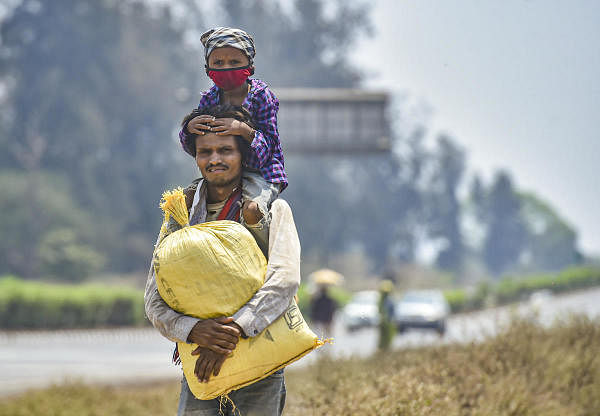A migrant worker from Madhya Pradesh carries a child as he walks along the Mumbai-Ahmedabad highway, following the coronavirus lockdown, in Palghar, Monday, March 30, 2020. (PTI Photo/Mitesh Bhuvad)