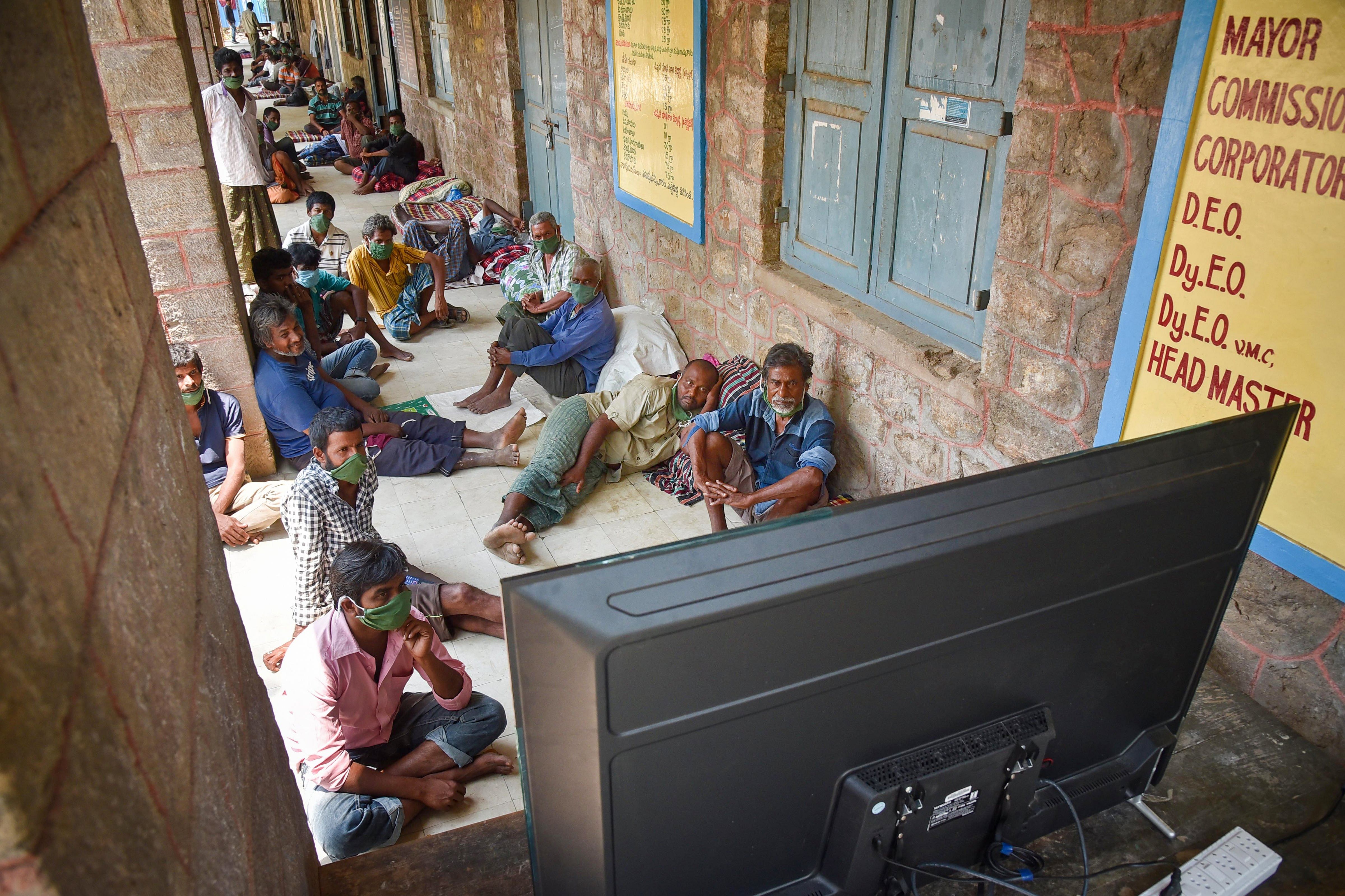 Homeless people watch TV at a makeshift shelter set up inside a school, during the nationwide lockdown. (Credit: PTI)