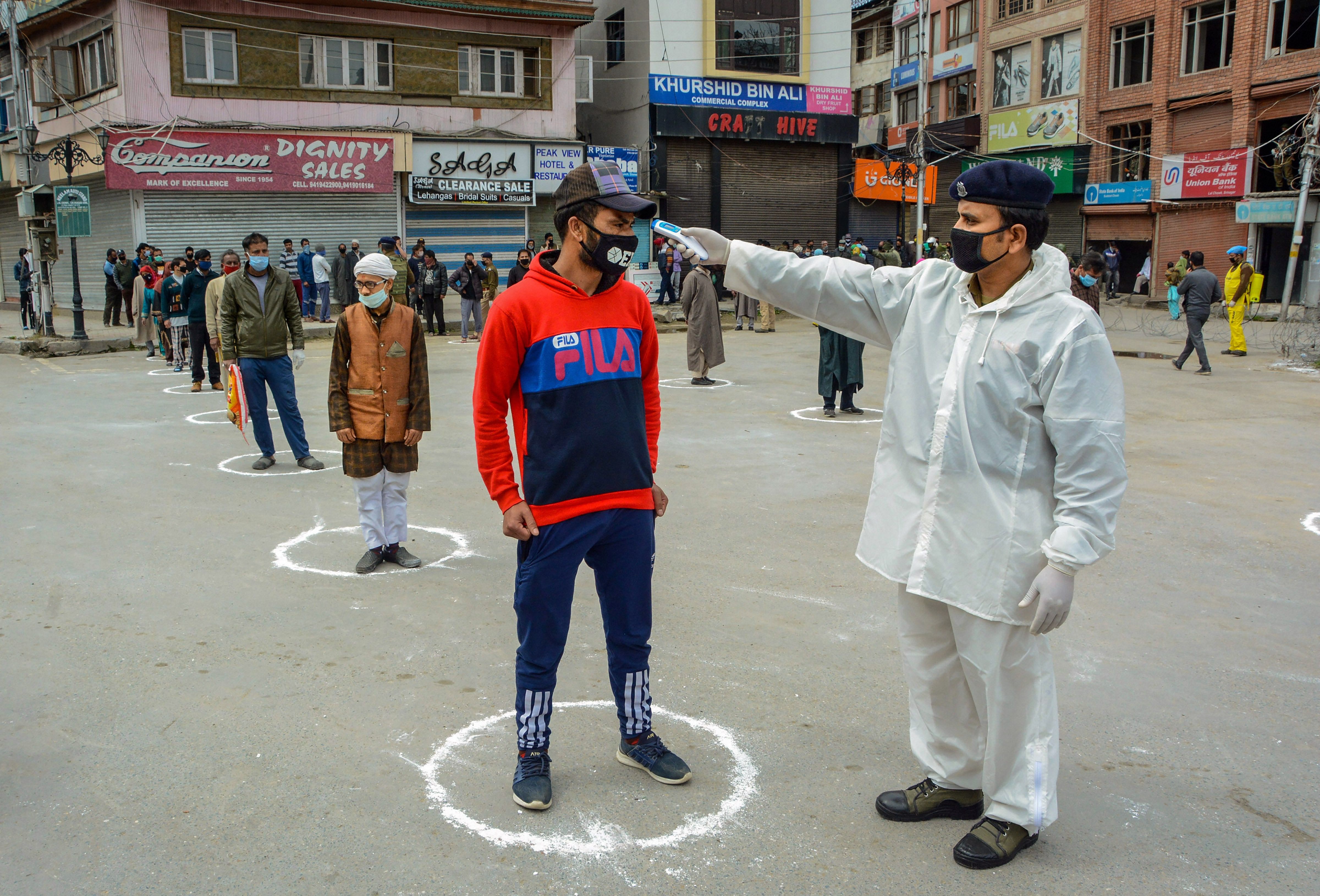 A CRPF doctor checks the temperature of residents as they wait in a queue to collect relief material being distributed by the force, during the coronavirus lockdown. (PTI Photo)