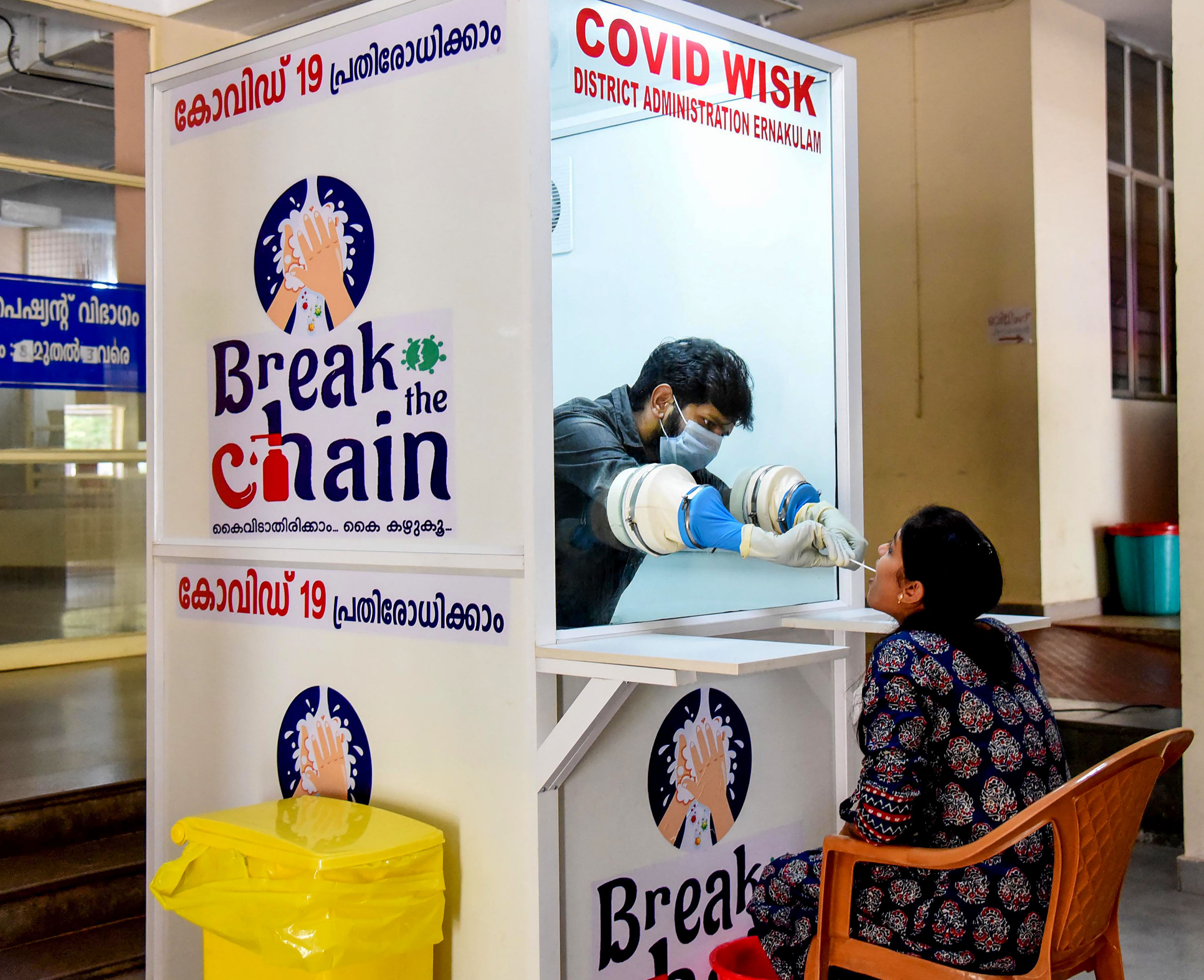 A medical staff member collects a swab sample of a woman for COVID-19 from the swab collection booth during the nationwide lockdown in the wake of coronavirus pandemic, at Government Medical College Ernakulam in Kochi. (Credit: PTI Photo)