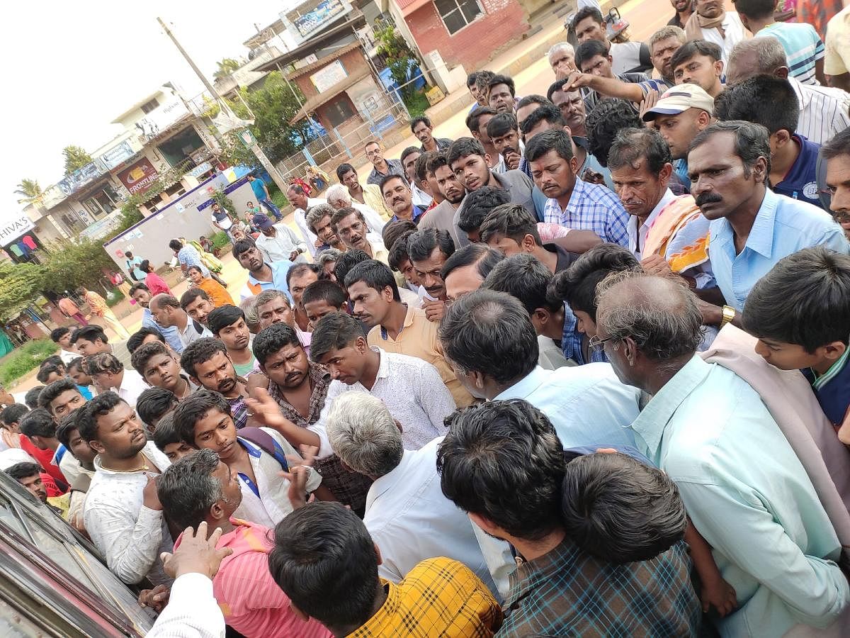 Passengers exchange heated words with vigilance squad members at Nittur bus stand in Gubbi taluk on Saturday. DH Photo