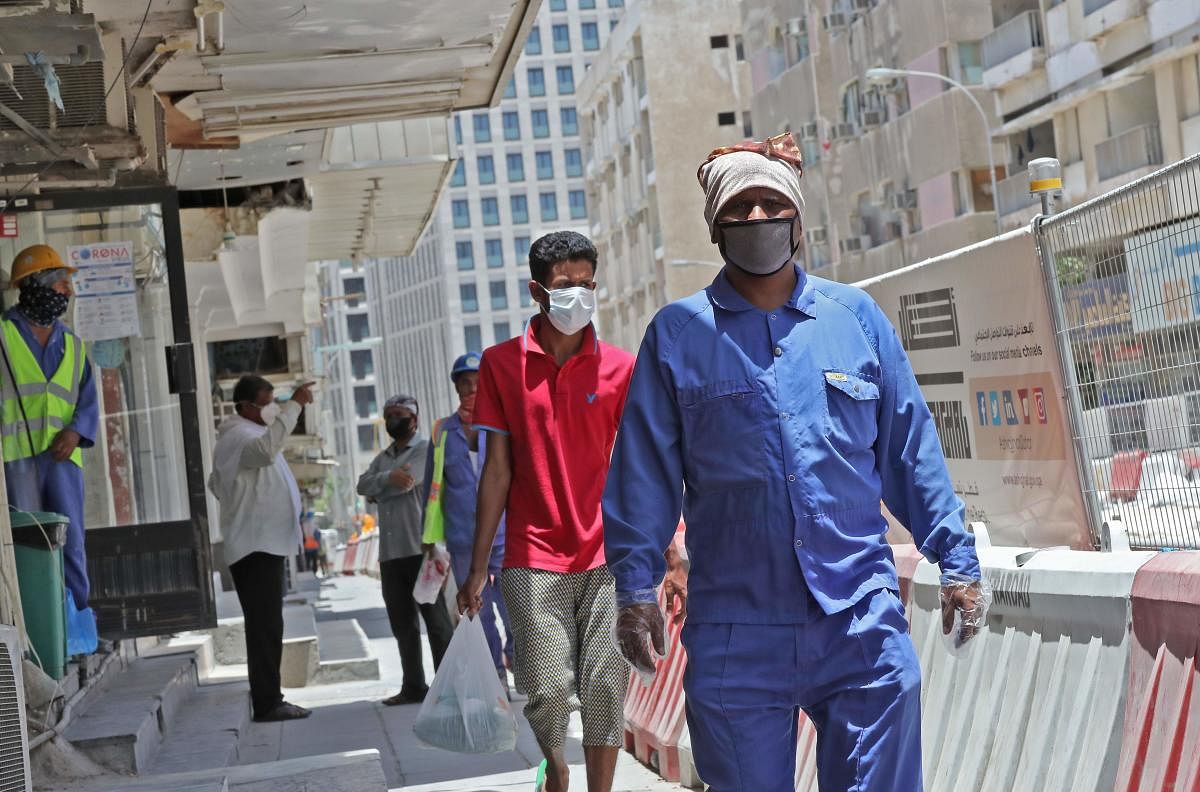 Workers wearing protective masks walk by on a street in Qatar (AFP Photo)