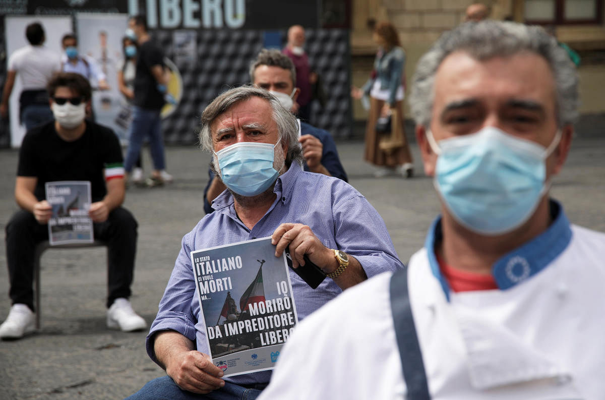 Business owners wearing protective face masks sit as they hold signs during a protest against restrictions set by the government to prevent the spread of the coronavirus disease (Reuters Photo)