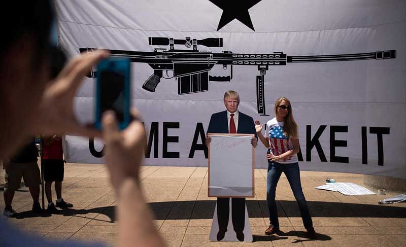 Bill Wang photographs his wife Brooke Wang as she sets a cardboard cutout of U.S. President Donald Trump in front of a banner during an open carry firearm rally on the sidelines of the annual National Rifle Association (NRA) meeting in Dallas, Texas, U.S., May 5, 2018. REUTERS