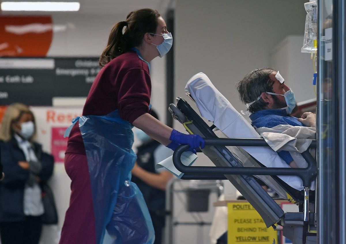 A medical professional in PPE, including gloves, an apron and a face mask as a precautionary measure against Covid-19, pushes a patient, also wearing a facemask, as he lays on a bed, inside St Thomas' Hospital in north London, on April 1, 2020. Credit: AFP Photo