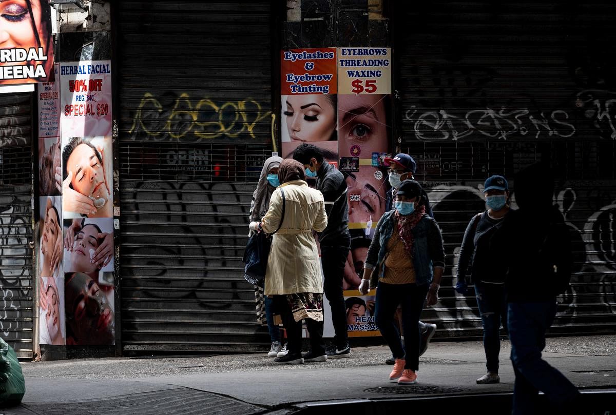 People wear face masks as they pass a closed beauty salon on May 18, 2020 in the Elmshurst neighbourhood of Queens in New York City. Credit: AFP Photo