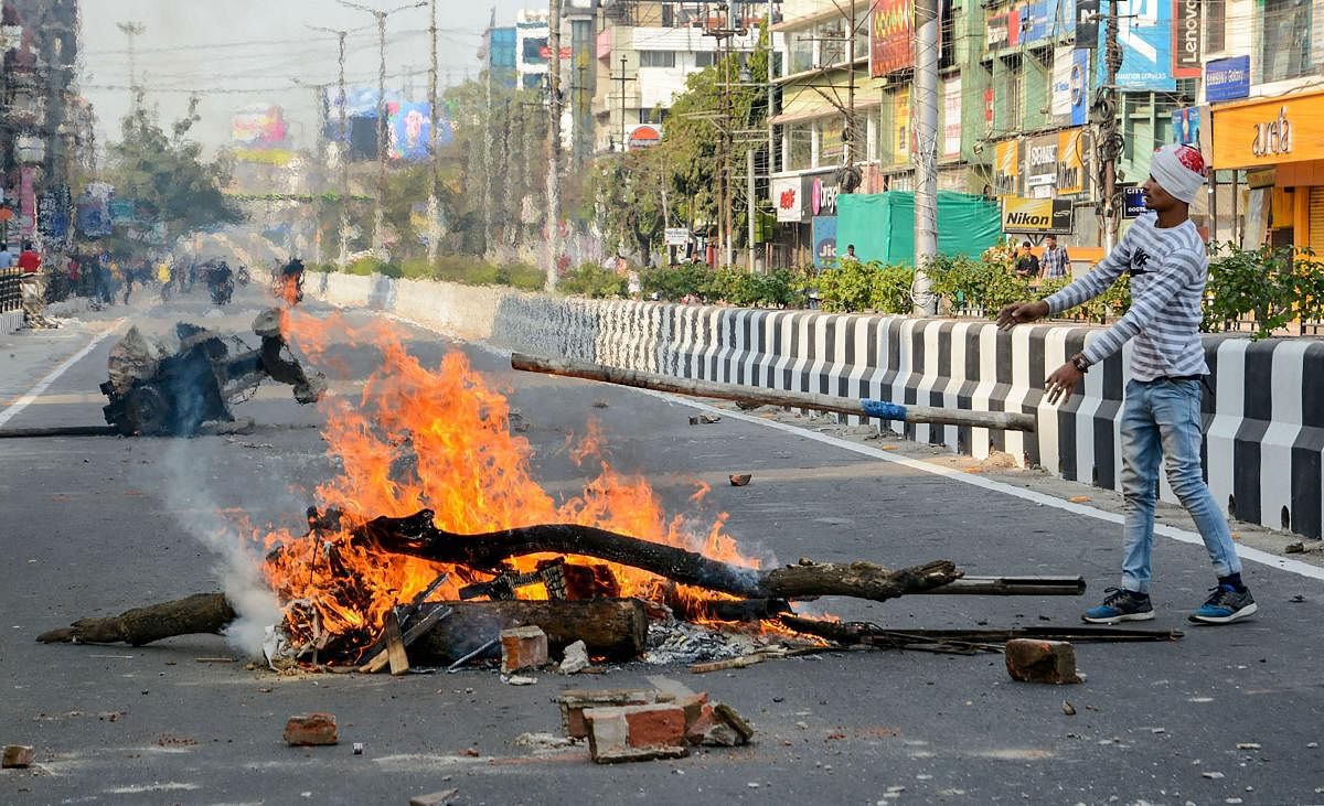 A protestor adds a log to a fire as he blocks a road, during an agitation against the Citizenship Amendment Bill, in Guwahati. PTI