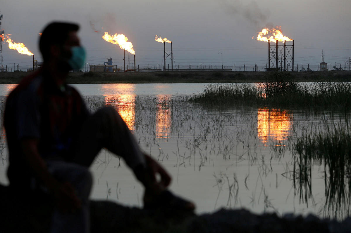 Flames emerge from flare stacks at Nahr Bin Umar oil field, as a man is seen wearing a protective face mask , following the outbreak of the coronavirus, north of Basra. Credit: Reuters File Photo