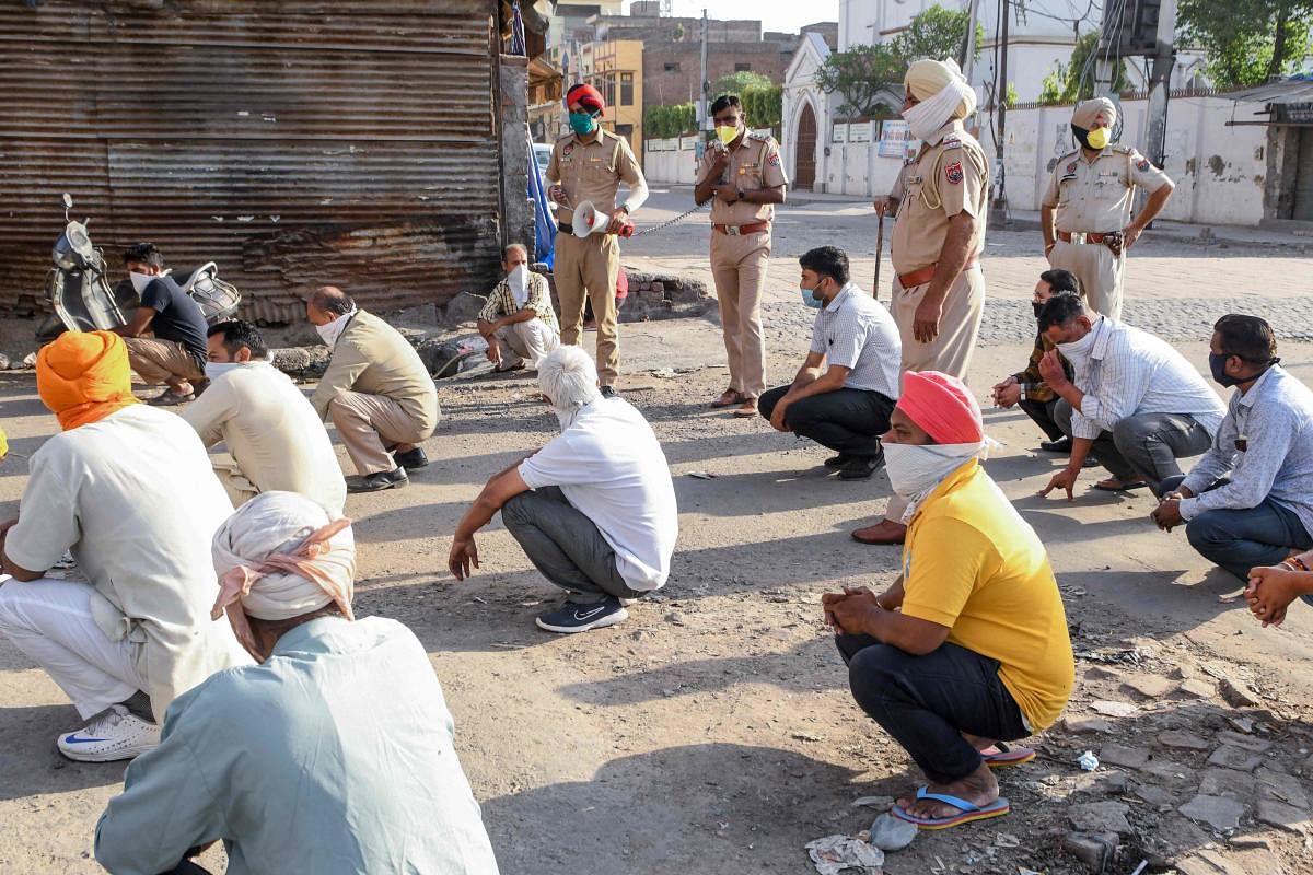 Police personnel (background) make people do squats as a punishment for breaching the lockdown restrictions (AFP Photo)