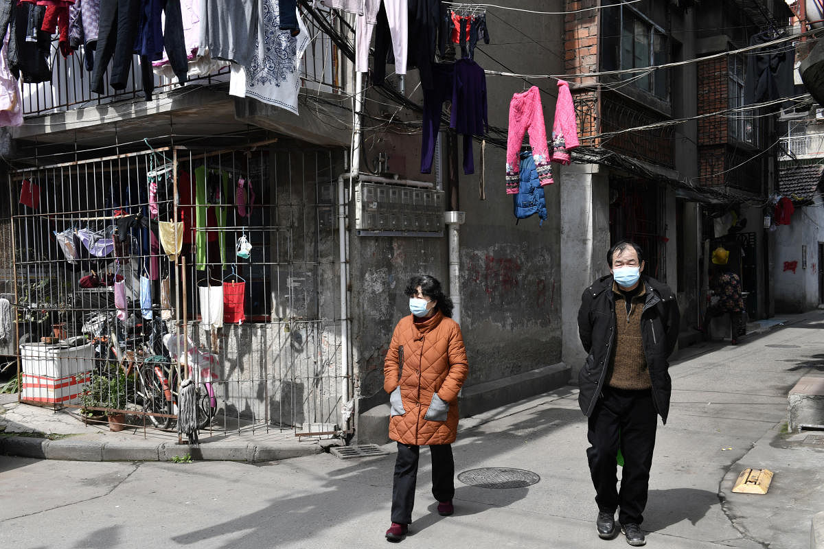 People wearing protective face masks walk past laundry hanging outside a house at a residential area in Wuhan. Credit: Reuters Photo