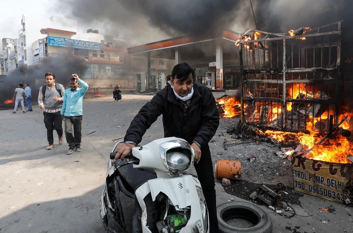 A man pushes his damaged scooter past a burning petrol pump during a clash between people supporting a new citizenship law and those opposing it, in New Delhi. Reuters