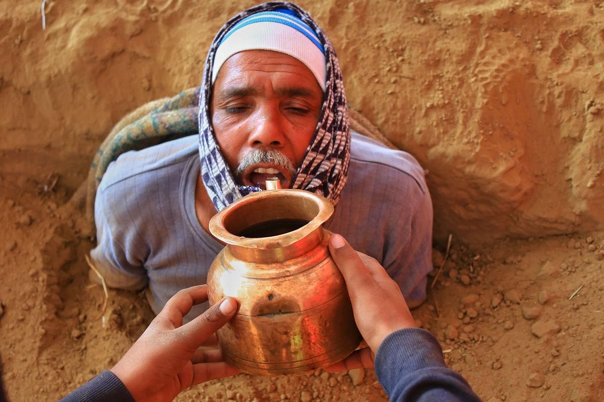 A farmer, who has buried himself upto his chest in protest against acquisition of his land, being offered water, at Nindar Village in Jaipur, Rajasthan. (PTI Photo)