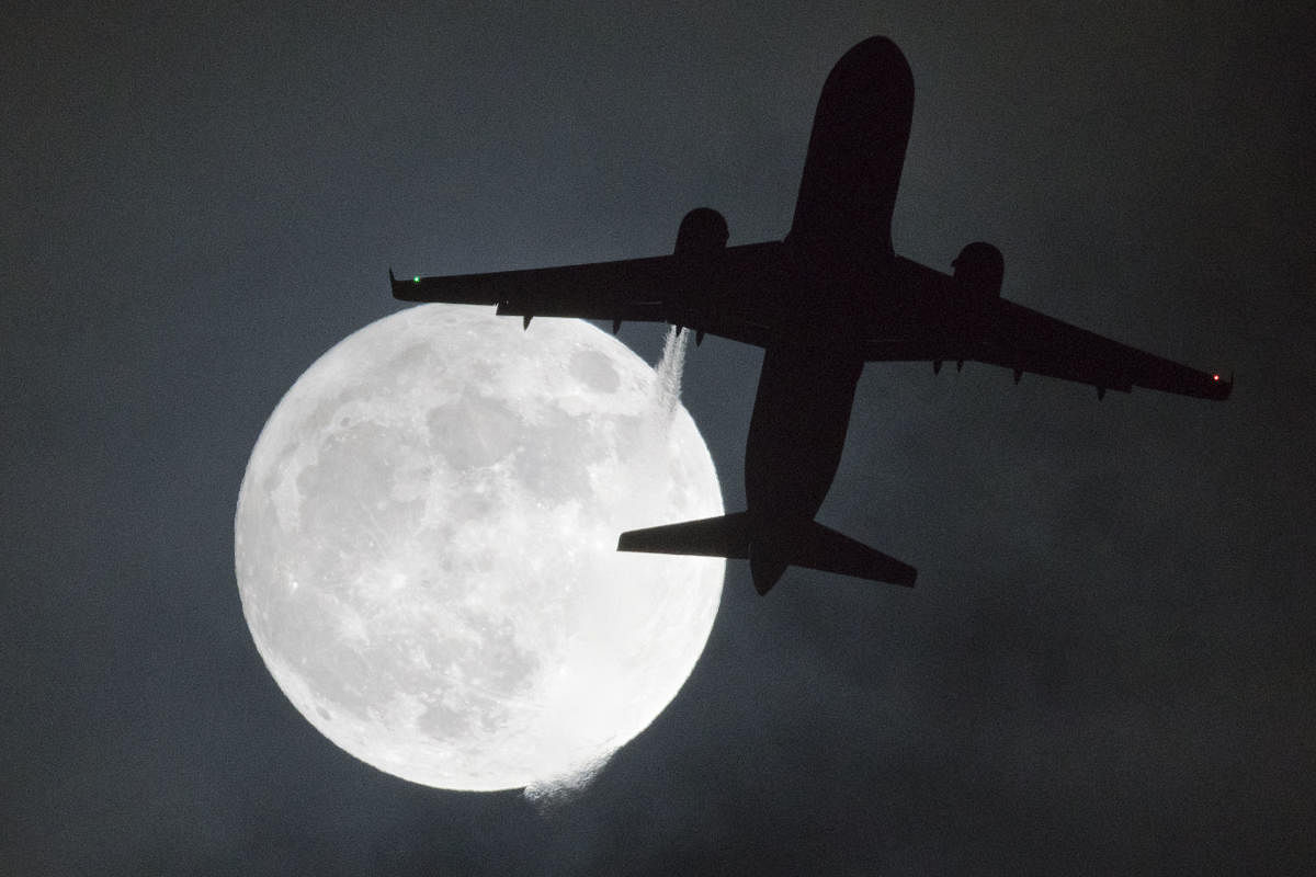 A plane flys in front of a "super moon" or "wolf moon" on its approach to London Heathrow Airport on January 1, 2018. / AFP PHOTO / Justin TALLIS