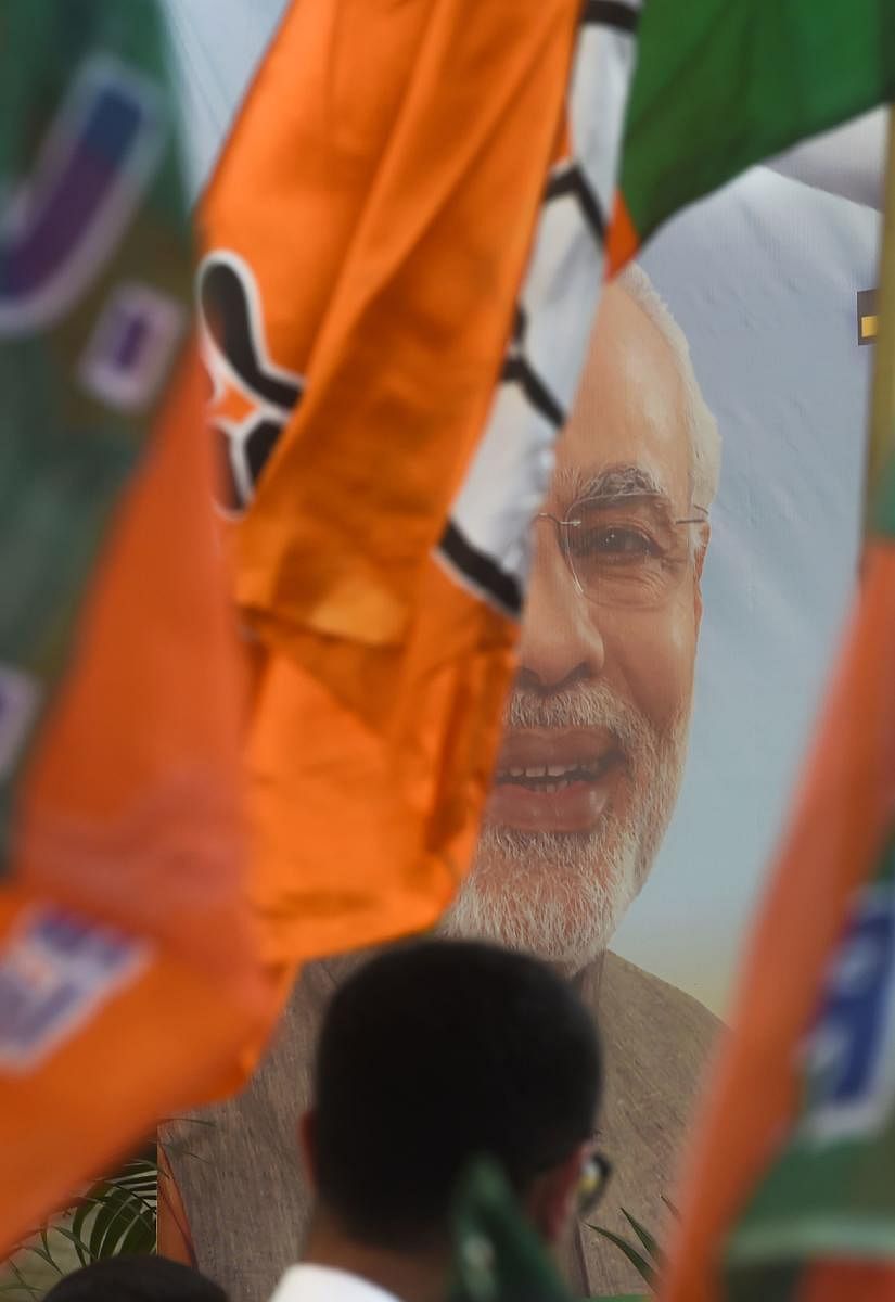 BJP workers carry flags past a poster of PM Narendra Modi during an event to celebrate the reservation bill passed in the Parliament, in Mumbai on January 1. AFP