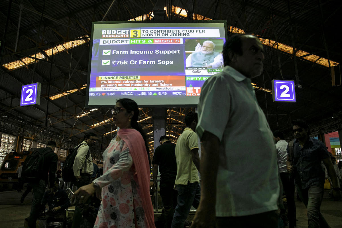India's Prime Minister Narendra Modi is seen as commuters walk past a screen telecasting the interim budget speech at a railway station in Mumbai. (REUTERS)