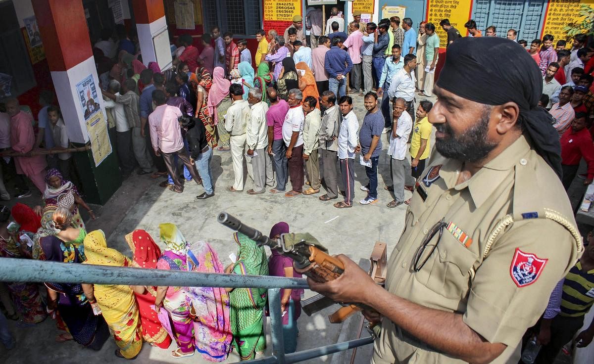 A security personnel stands guard as voters queue to cast their vote during the first phase of general elections, at a polling station in Meerut on Thursday. PTI