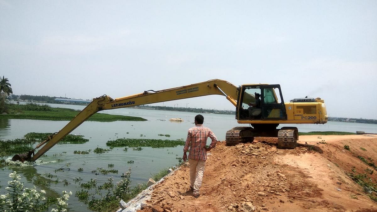 Water in Lakshmisagar Lake at Narasapura in Kolar taluk has already turned green. An excavator removes hyacinth from the water on Friday. dh photo/chiranjeevi kulkarni
