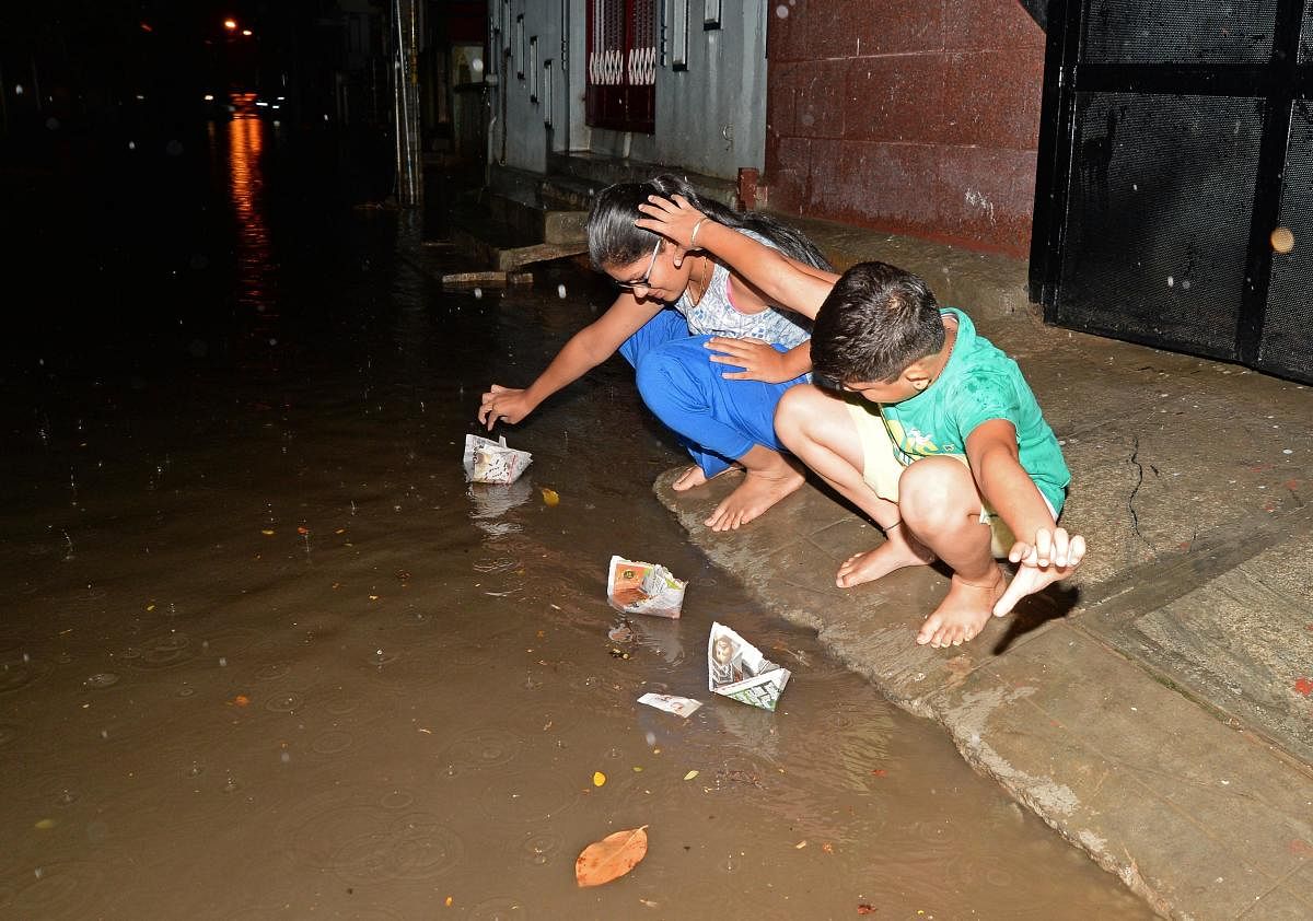 Children float paper boats on a waterlogged Malleswaram Link Road on Tuesday night. A large tree fell on the road near NTTF Circle in Peenya on Tuesday. 