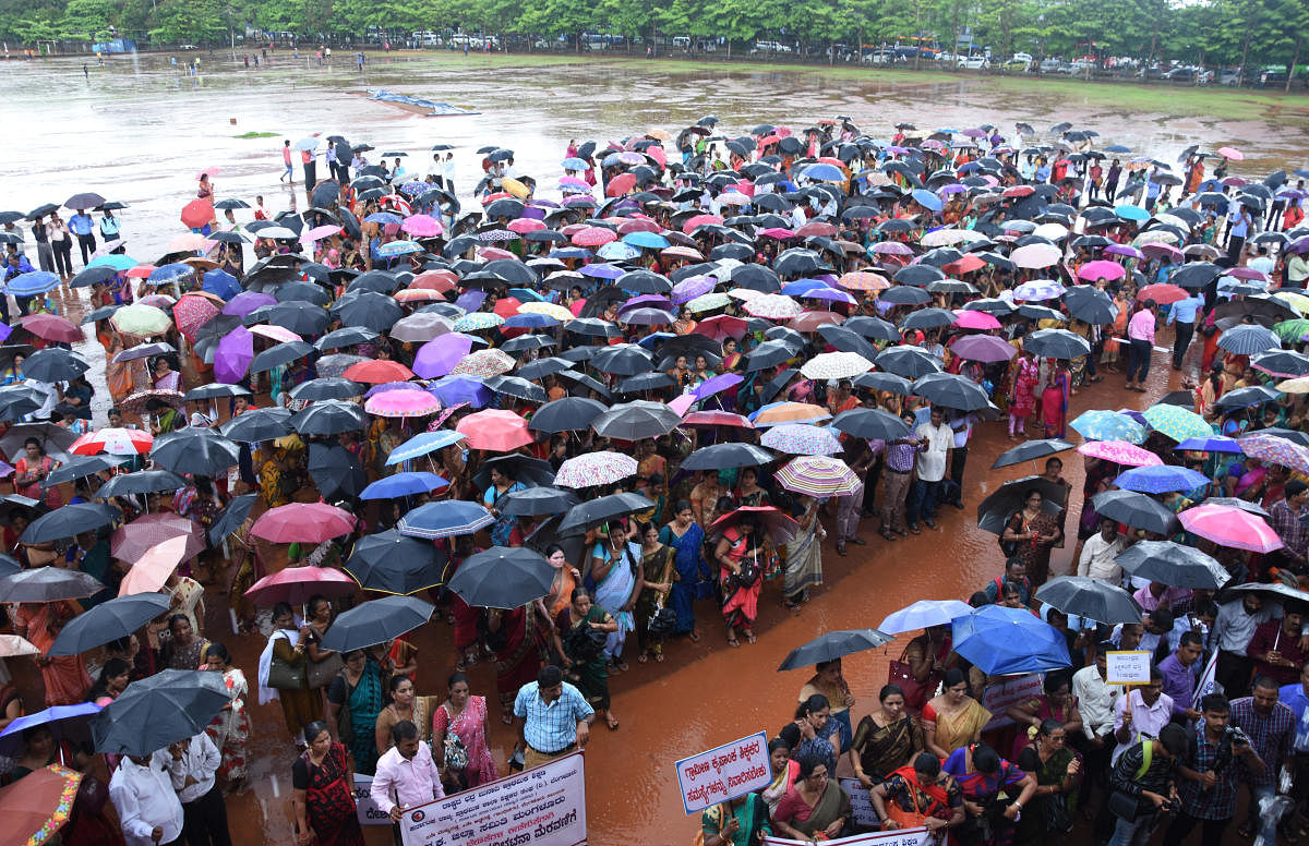 Teachers hold umbrellas to protect themselves from rain during a protest staged at Nehru Maidan in Mangaluru on Tuesday.
