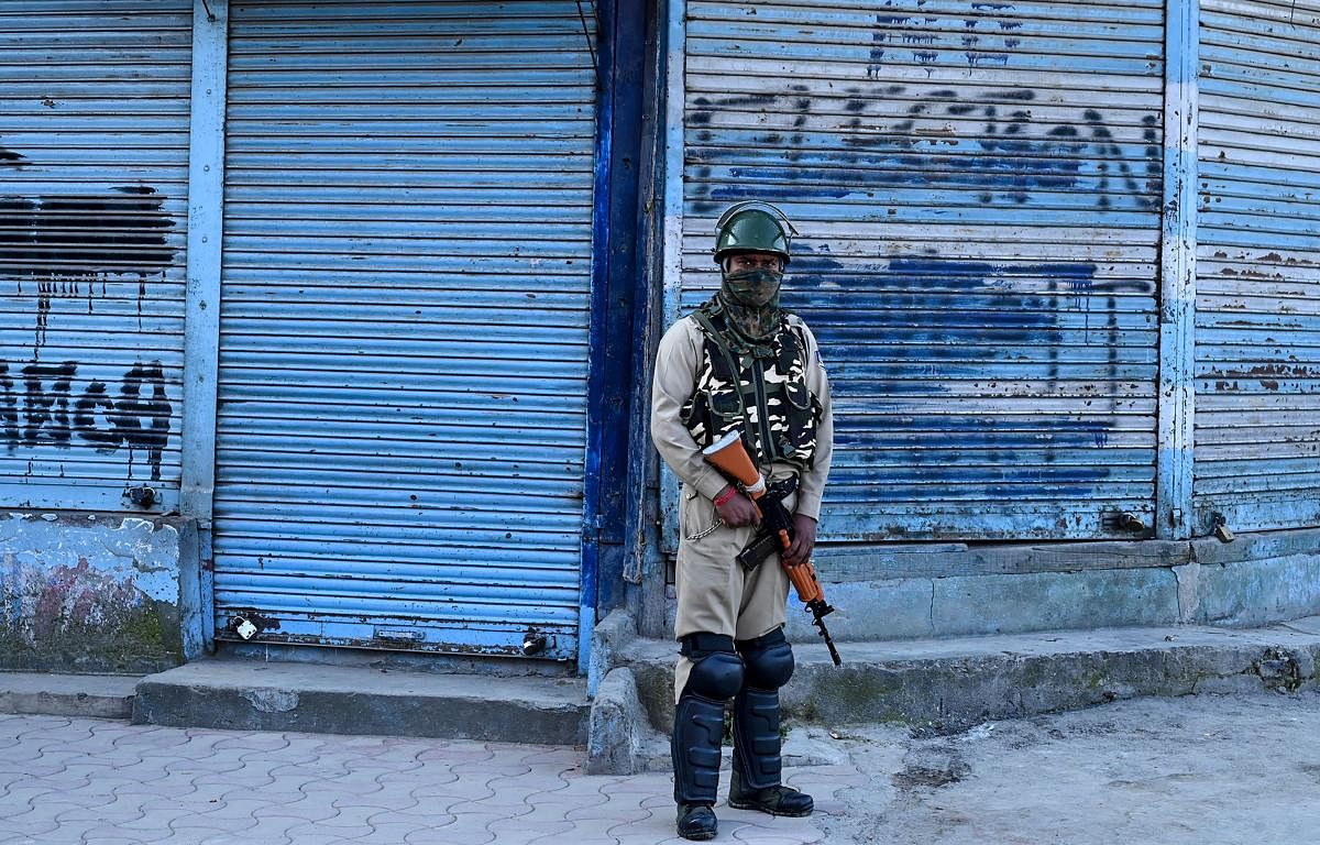 A security personnel stands guard in front of closed shops in Srinagar. AFP file photo