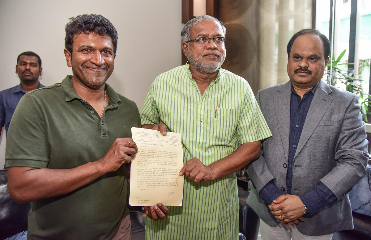 Chamarajanagar District Minister S Suresh Kumar hands over a letter to Sandalwood star Puneeth Rajkumar appointing him the Development Ambassador of the district, in Bengaluru on Saturday. Deputy Commissioner of Chamarajanagar M R Ravi looks on. DH PHOTO/