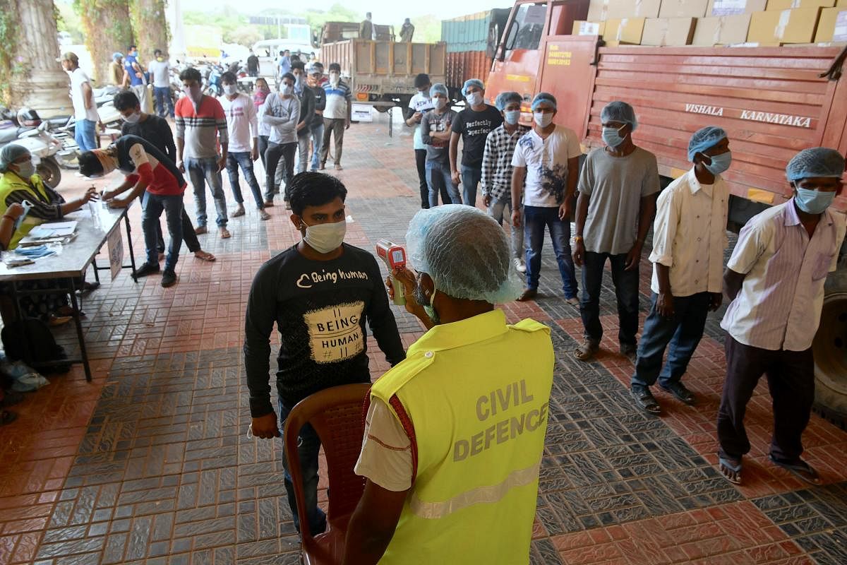 A volunteer (C) gets his temperature checked as others sign up and stand in a queue before entering a warehouse to pack emergency essentials and groceries to be distributed to needy people in Bengaluru on Monday. AFP