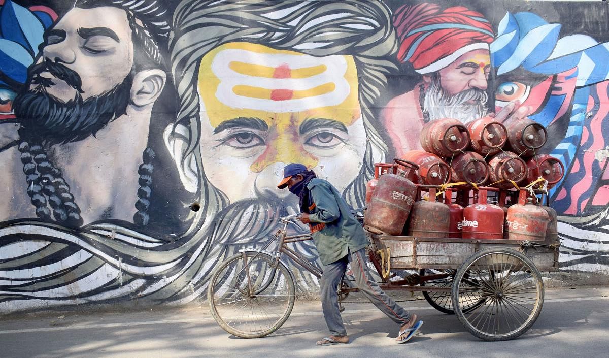 Delivery man carrying LPG cylinders walks past graffiti during the lockdown to curb coronavirus spread. (PTI Photo)