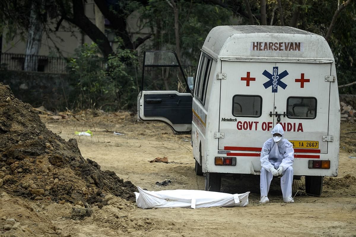 A health worker wearing protective gear sits on an ambulance next to the dead body of a Covid-19 victim at a graveyard in New Delhi on May 13, 2020. AFP