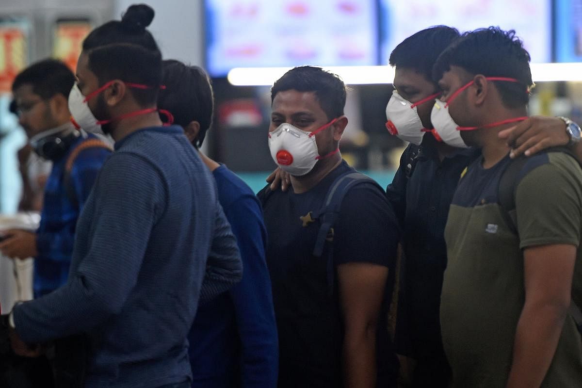 Passengers wearing facemasks amid concerns over the spread of the COVID-19 novel coronavirus, stand in a queue at a counter inside the airport in Goa. AFP