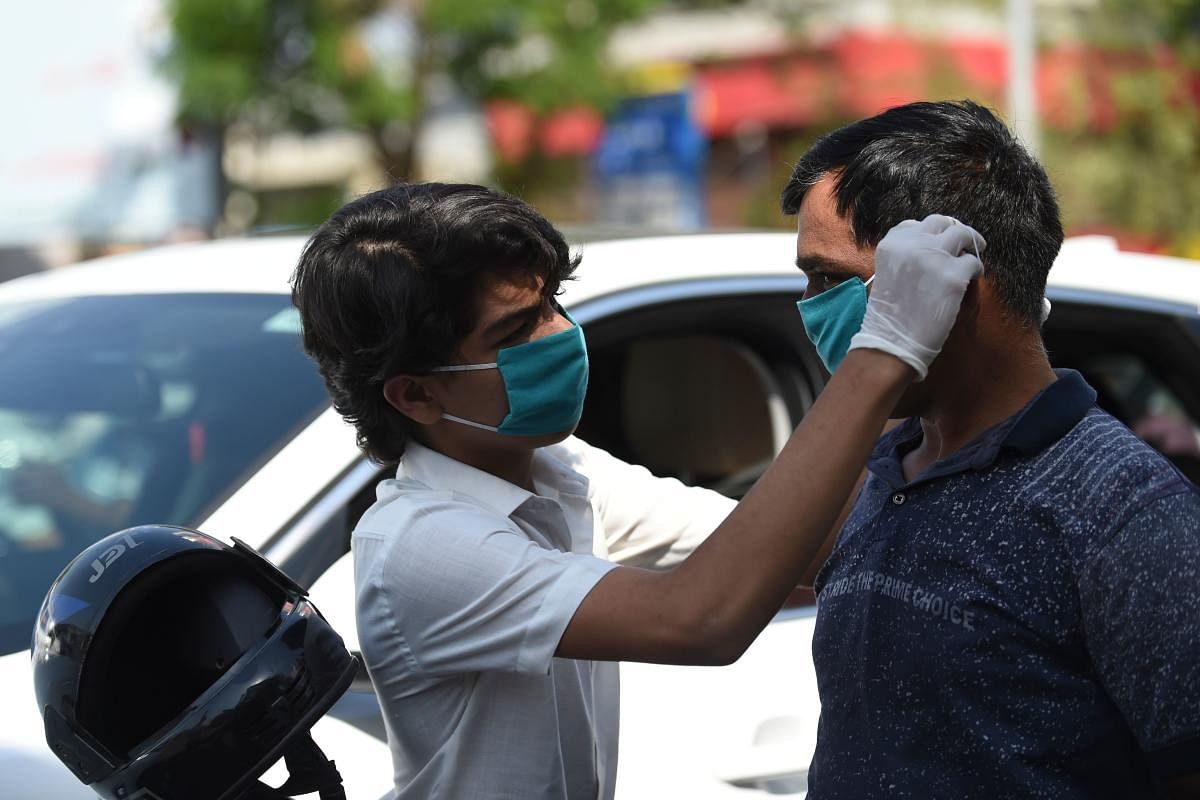 A volunteer of the Humf NGO adjusts a free facemask to a motorist during a facemaks donation campaing amid concerns over the spead of the COVID-19 coronavirus, in Ahmedabad on March 17, 2020. Credit: AFP Photo