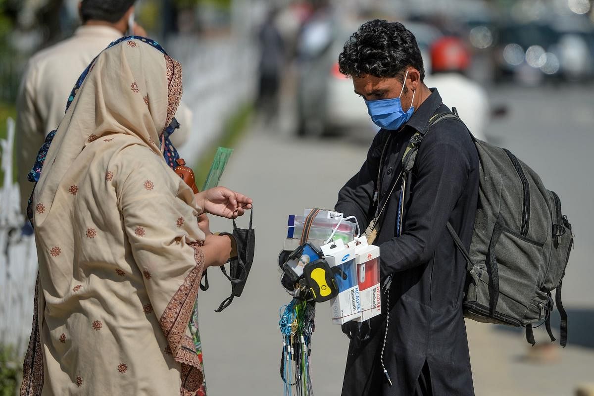 A street vendor (R) wearing a facemask as a preventive measure against the COVID-19 coronavirus, interacts with customers alongside a street in Islamabad on March 19, 2020. Credit: AFP Photo