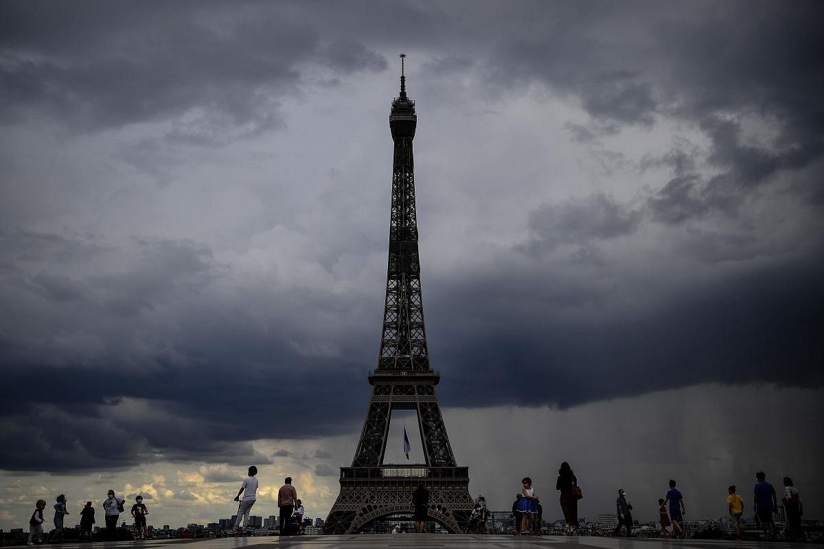 People gather on the Trocadero Esplanade as dark rain clouds loom over The Eiffel Tower in Paris. AFP