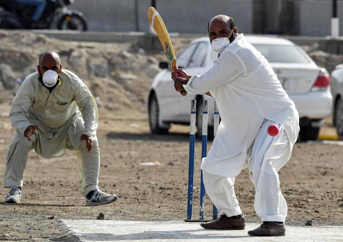 Foreign workers in the United Arab Emirates of Pakistani origin, wearing face masks as protection from COVID-19 coronavirus disease, play cricket for leisure at a pitch in the centre of the emirate of Sharjah on March 20, 2020, despite government instructions to limit public gatherings. Credit: AFP Photo