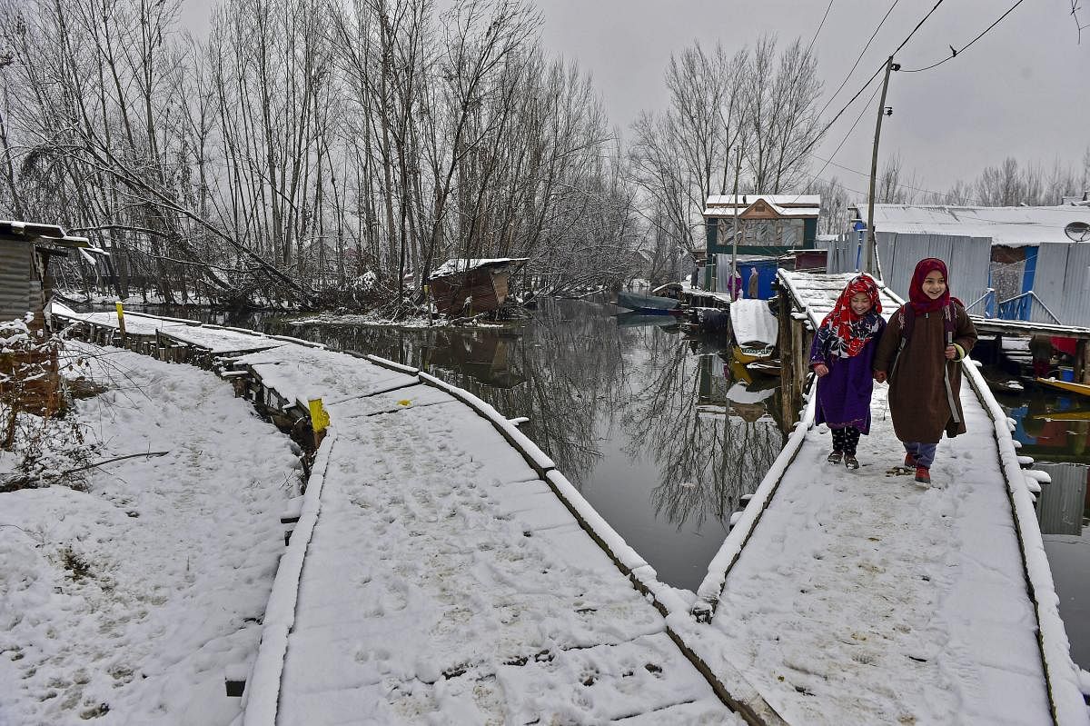 Young girls walk over a snow-laden wooden bridge after a light snowfall, in Srinagar. PTI