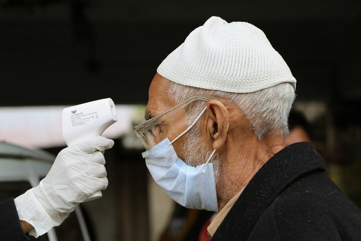 A doctor checks temperature of a passenger stranded near a bus stand during day-3 of the nationwide lockdown, imposed in the wake of coronavirus pandemic, in Jammu, Friday, March 27, 2020. (PTI Photo) 