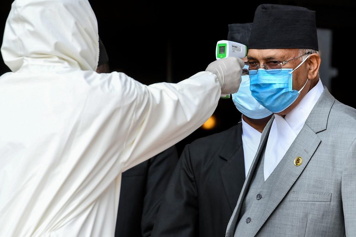 A health worker in protective gear checks the body temperature of Nepal's Prime Minister KP Sharma Oli (R) as he arrives at the parliament. AFP