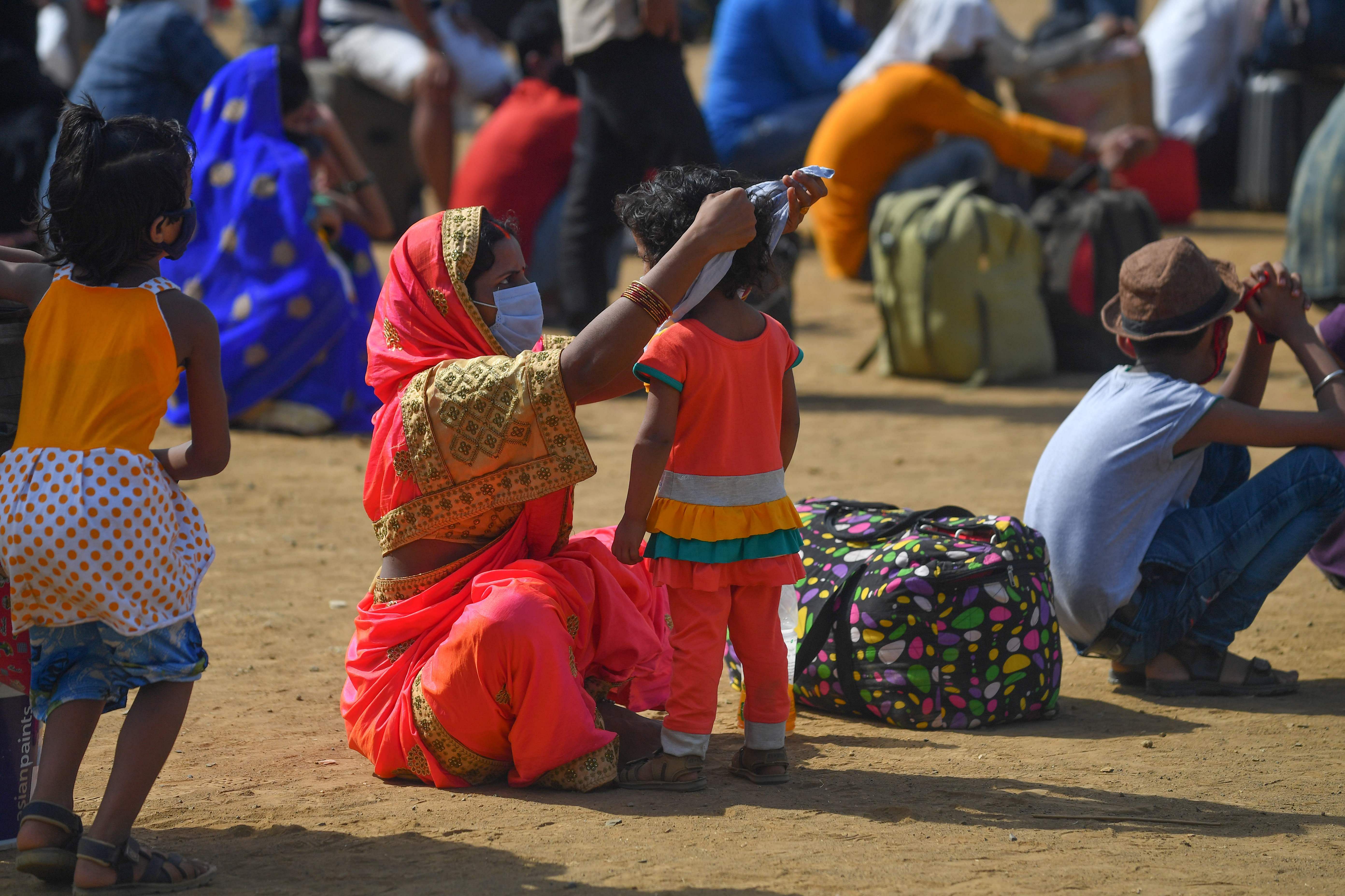 A mother ties a handkerchief around her child's face while waiting in a park along with other migrant workers for transportation to a nearby railway station. (AFP Photo)