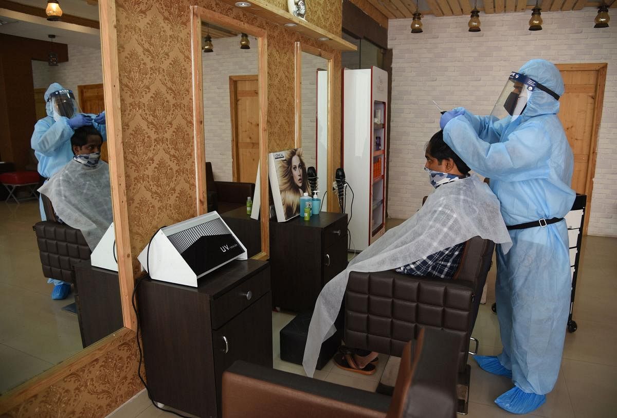 A barber wearing personal protective equipment (PPE) gives a haircut to a customer, during the fourth phase of the ongoing nationwide COVID-19 lockdown, in Bengaluru, Thursday, May 21, 2020. Credit: PTI Photo
