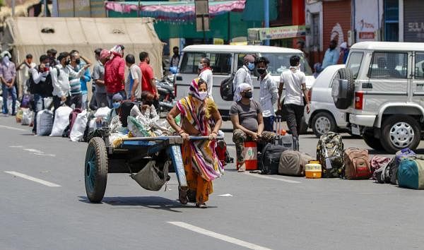 A woman, foreground, pulls a cart as migrant workers wait for means of transport to reach their native places, during the fourth phase of the ongoing COVID-19 nationwide lockdown, in Ahmedabad, Thursday, May 21, 2020. (PTI Photo)
