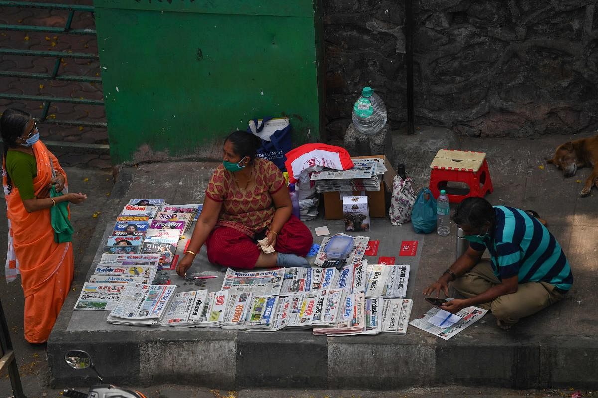 A woman selling newspapers interacts with a customer during a government-imposed nationwide lockdown as a preventive measure against the spread of the COVID-19 coronavirus in Mumbai on April 27, 2020. Credit: AFP Photo