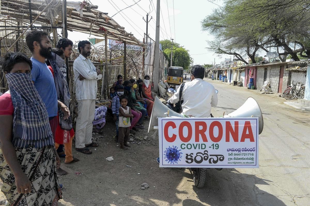 Farmer Bamandla Ravinder, who tours on his bike in the villages of Telangana state to spread awareness about the COVID-19 coronavirus, rides as people stand watching him in the slums in Hyderabad on May 21, 2020.  Credit: AFP Photo