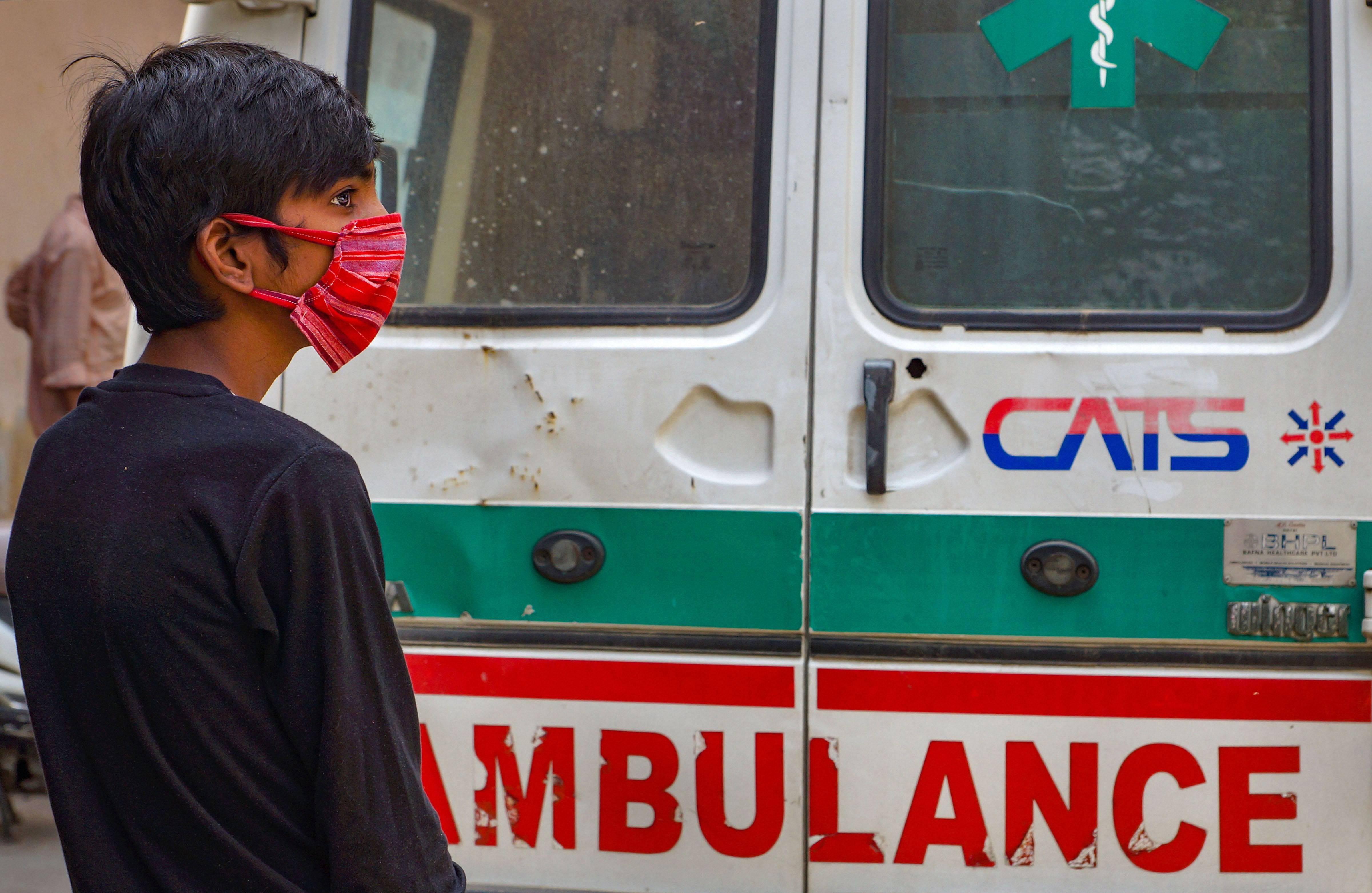 A suspected COVID-19 patient, wearing a mask, stands near an ambulance before being taken to a hospital for quarantine in East Delhi. (PTI photo)