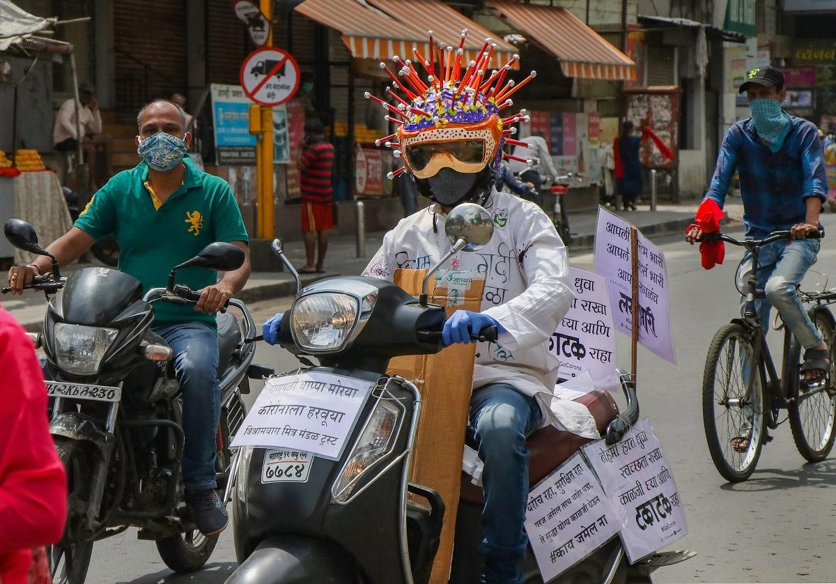 A man wearing a coronavirus theme-based helmet rides a scooter with placards on it to spread awareness among people, during the ongoing COVID-19 lockdown, at Tilak road in Pune, Tuesday, May 19, 2020. (PTI Photo)