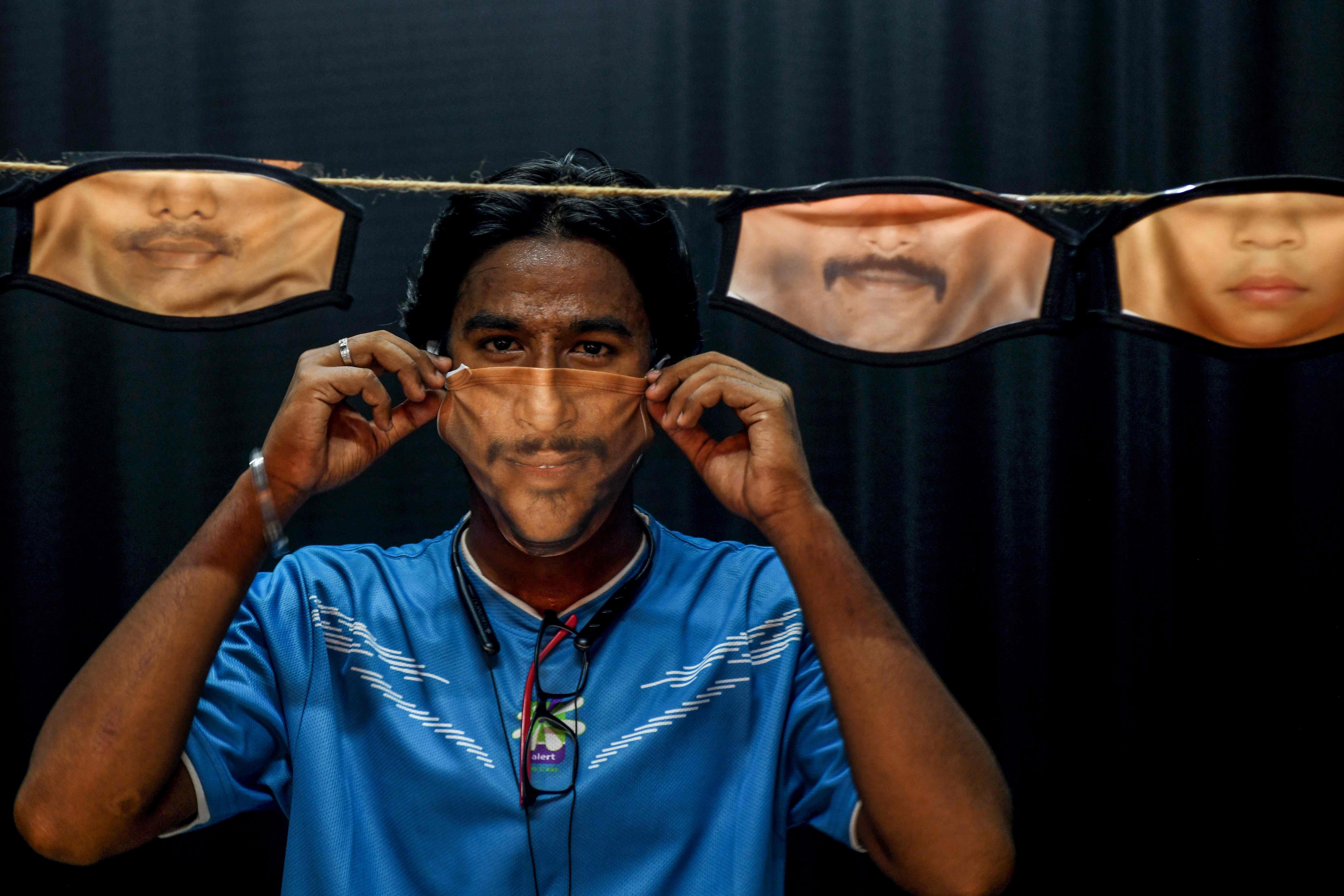 A man adjusts a facemask with his face's image printed on it created at a photo studio as other facemasks are hung amid concerns over the spread of the COVID-19 coronavirus in Chennai. (AFP photo)