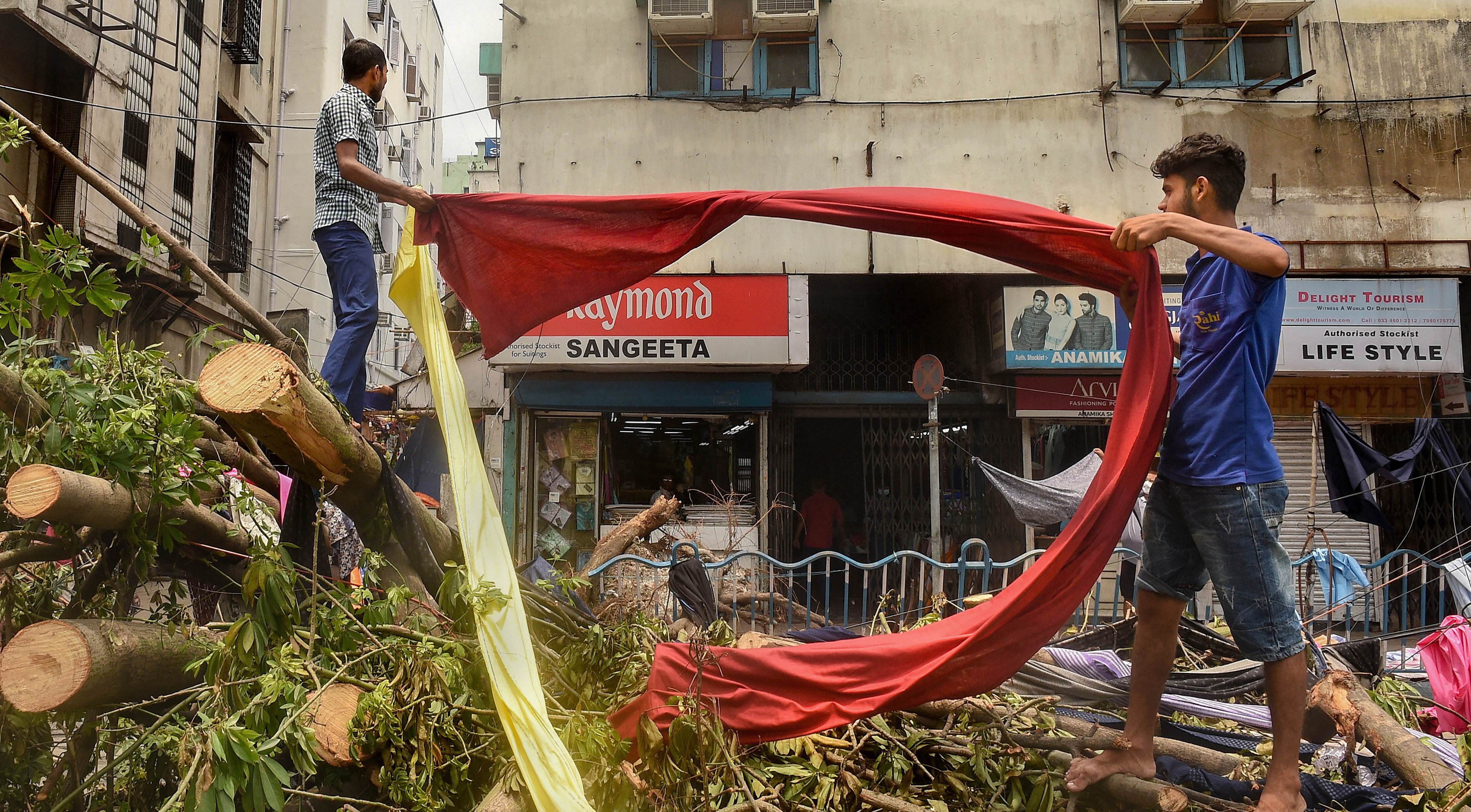 Shopkeepers dry a piece of cloth on an uprooted trees, in the aftermath of Cyclone Amphan. (PTI Photo)