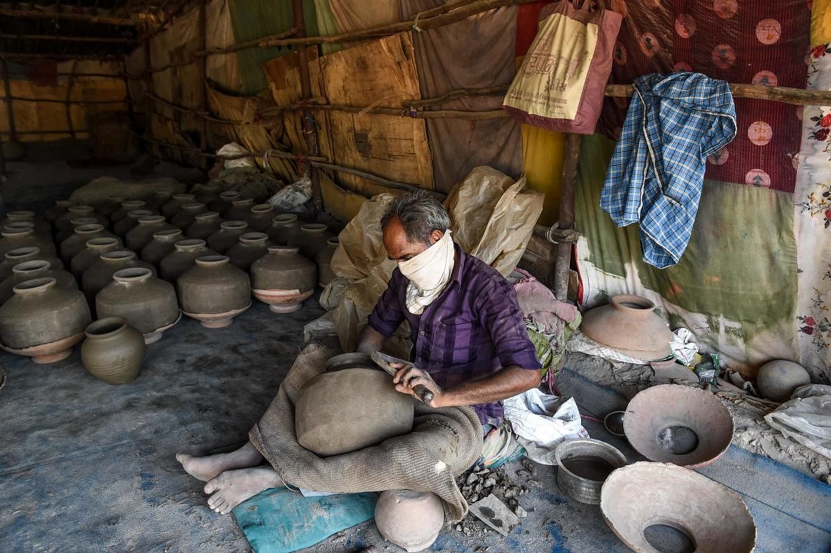 A potter works on earthen pots made for water storage in Ahmedabad on May 20, 2020. (Photo by SAM PANTHAKY / AFP)