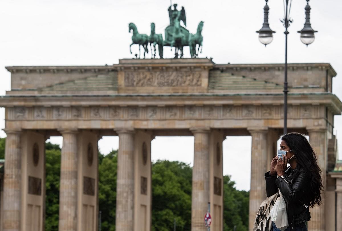 A woman puts a face mask on before entering a coffee shop in front of the Brandenburg Gate in Berlin. (AFP Photo)